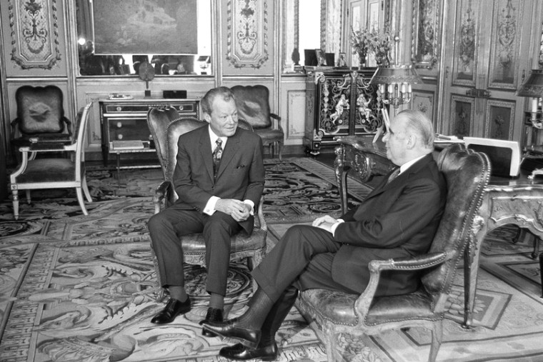 Willy Brandt sitzt neben dem französischen Staatspräsidenten Georges Pompidou in einem Zimmer des Élysée-Palasts. Fotografie in Schwarz-Weiß.