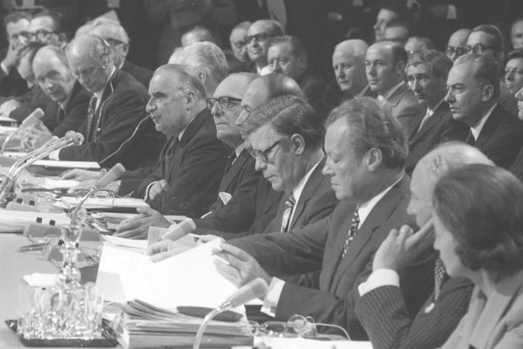 Schwarz-Weiß-Aufnahme des Gipfeltreffens der Staats- und Regierungschefs der Europäischen Gemeinschaft, u.a. mit Willy Brandt. Auf dem Tisch vor den Staats- und Regierungschefs sind Mikrophone und Bürounterlagen zu sehen. Dahinter sitzen Beamte.