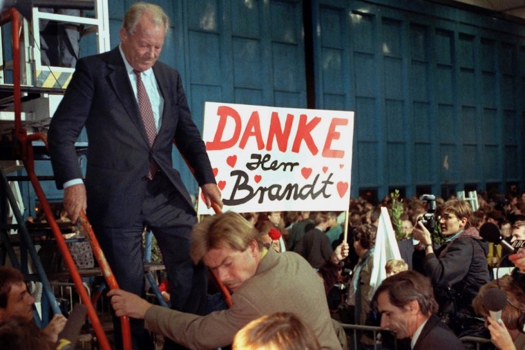 Willy Brandt steigt eine Treppe herunter, neben Ihm ist ein Plakat zu sehen, auf dem „Danke Herr Brandt“ steht.