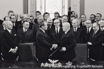 Willy Brandt und der polnische Ministerpräsident Józef Cyrankiewicz schütteln sich nach der Unterschreibung des Warschauer Vertrags die Hände. Fotografie in Schwarz-Weiß. Öffnet eine Sammlung verschiedener Videos und Interviews von Willy Brandt.