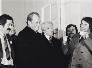 Willy Brandt steht zwischen Günter Grass und Walter Scheel. Schräg vor ihm spricht der Juso-Vorsitzende Wolfgang Roth. Fotografie in Schwarz-Weiß.