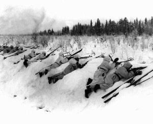 Schwarz-Weiß-Aufnahme aus dem Jahre 1939, auf der finnische Soldaten zu sehen sind, die neben ihren Skiern im Schnee liegen und durch ihre Gewehre blicken.
